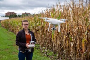 Graduate student Dorothy Kirsch operates a white drone on the University of Minnesota St. Paul Campus, in front of a corn field, uncovering predictive tools for corn management
