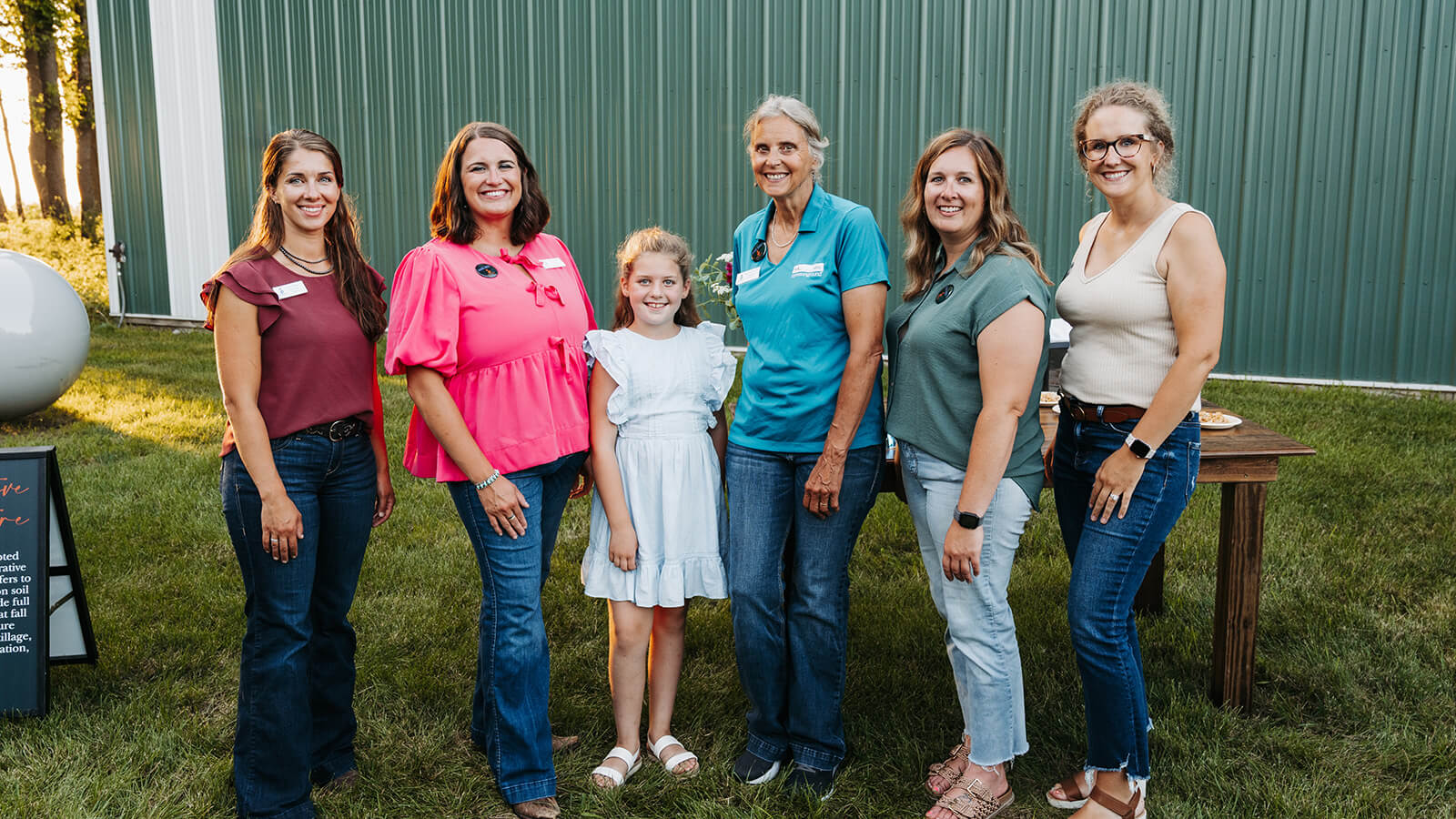 CommonGround Minnesota volunteers and attendees gather for a 2025 farm dinner event, smiling together outdoors beside a green barn.